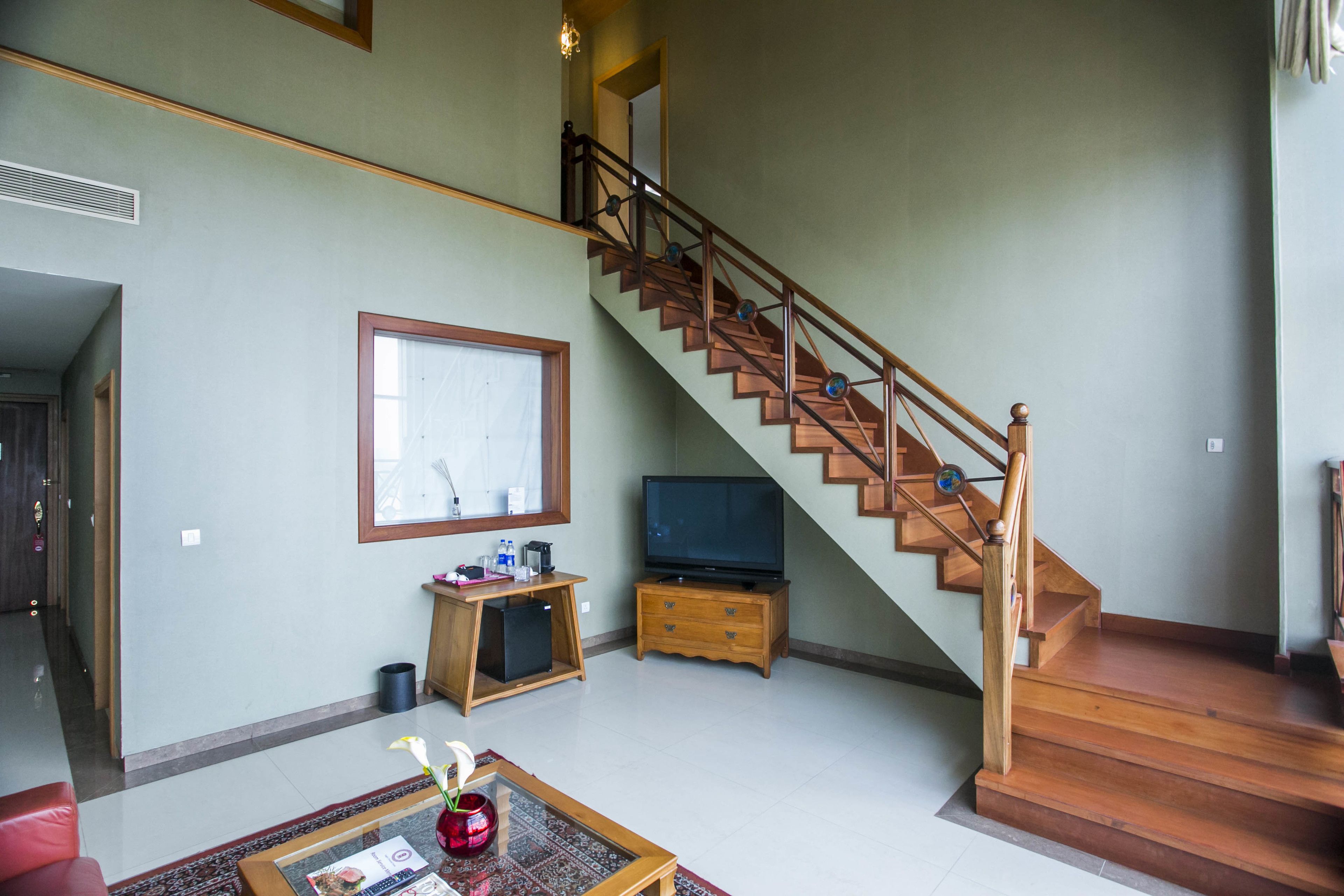 A spacious living area with a wooden staircase, a television on a wooden stand, and a framed picture on the wall.
