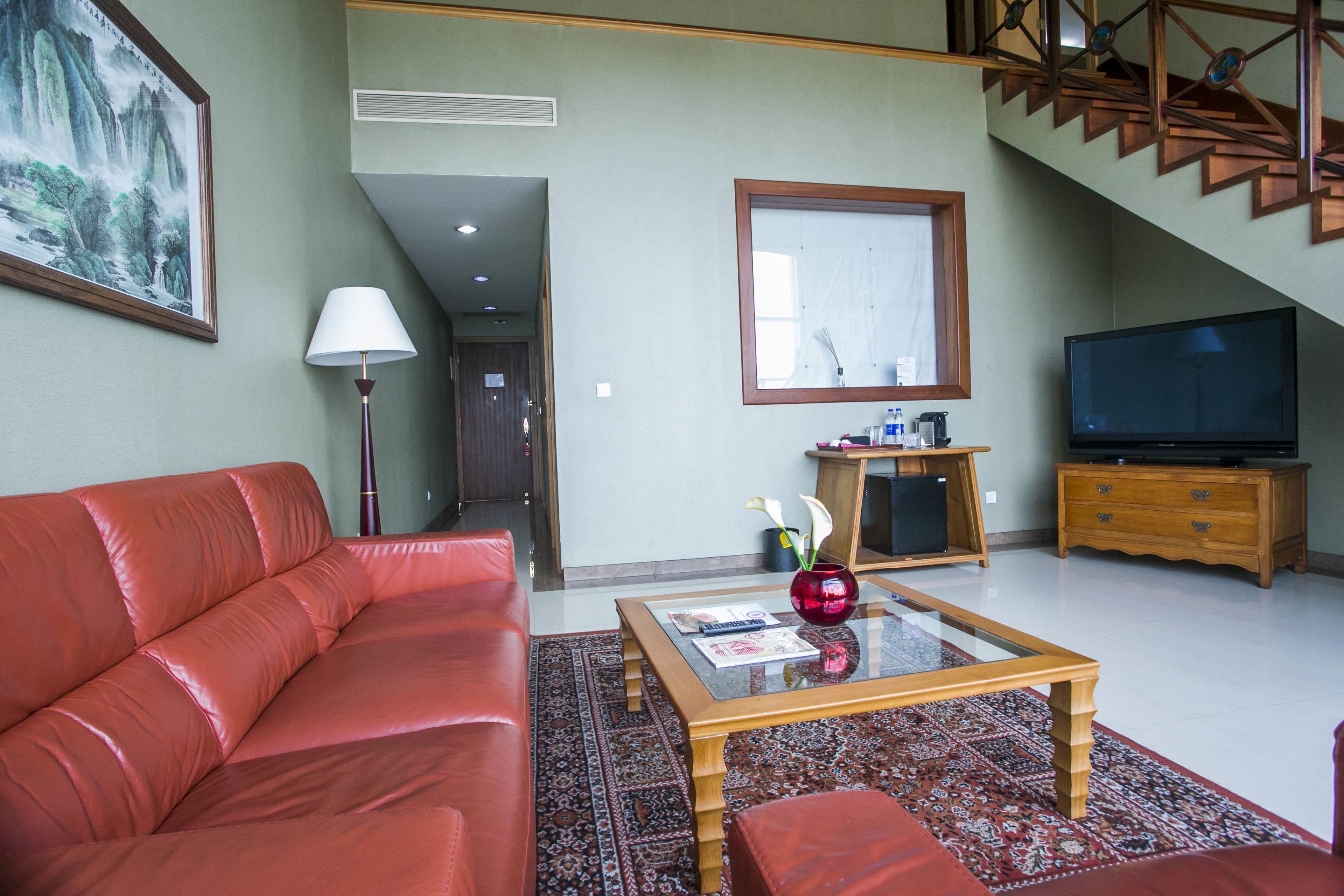 A living room with a red sofa, a glass coffee table, a wooden TV stand, and a painting on the wall.