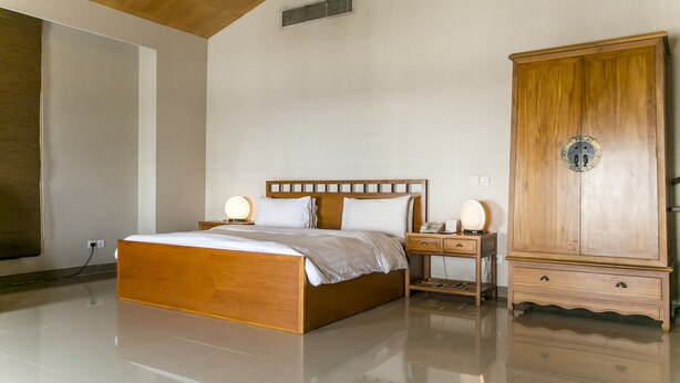 A bedroom with a wooden bed, bedside lamps, a wardrobe, and a wall-mounted vent. - Lagos Oriental Hotel (Lagos)