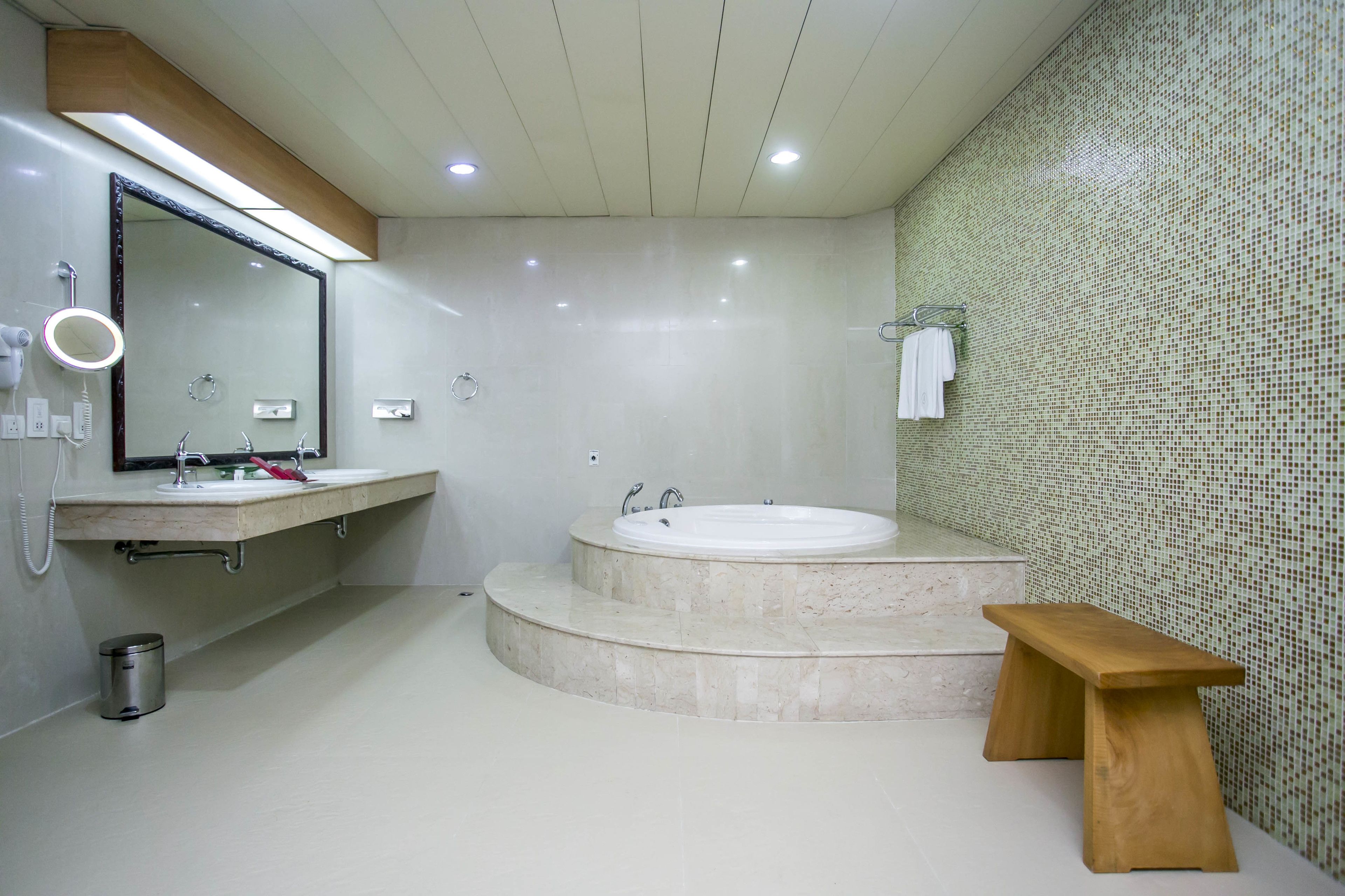 A modern bathroom with a large bathtub, a vanity with a mirror, and a wooden bench.