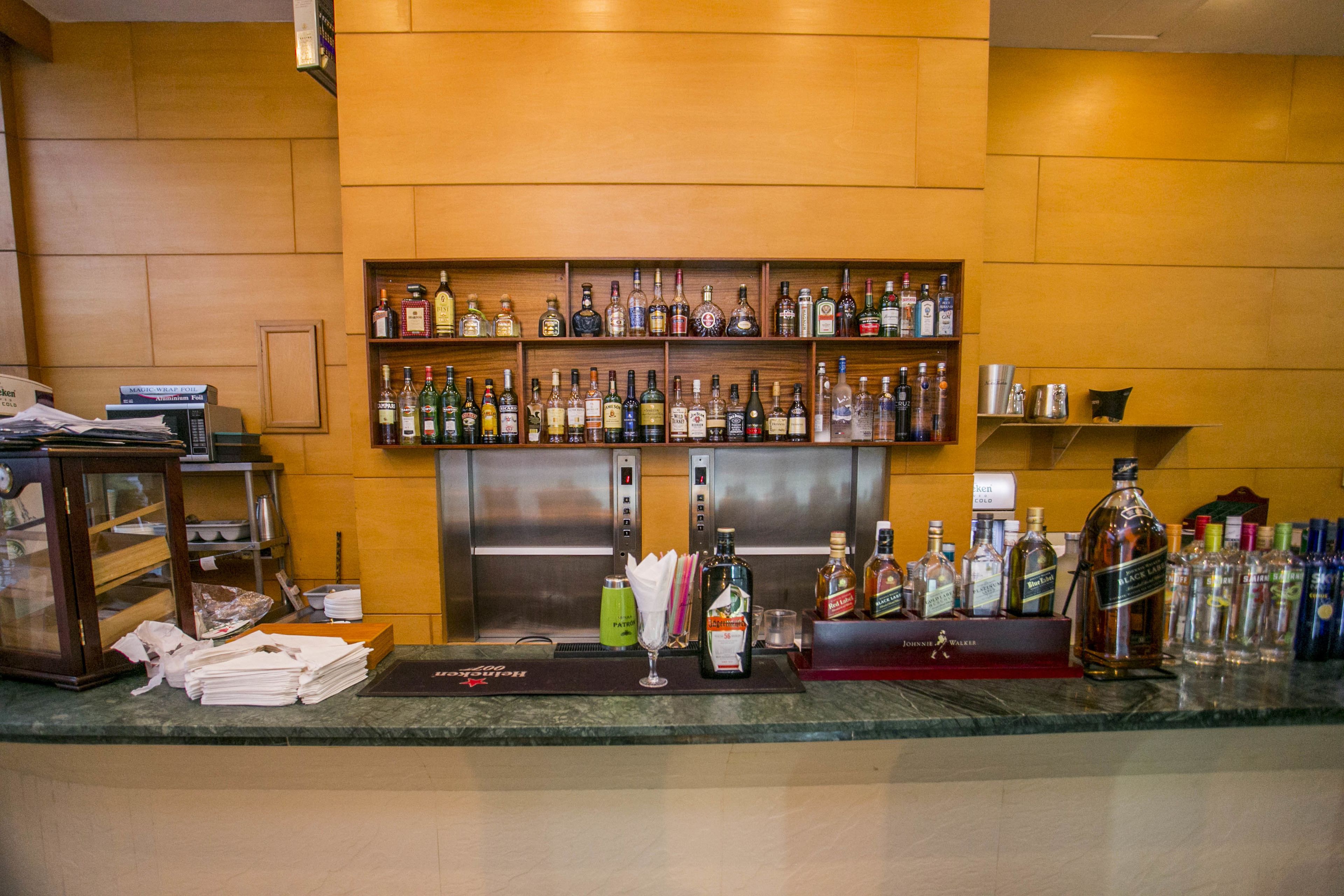 A bar area with shelves of liquor bottles, a cash register, and a bar counter.
