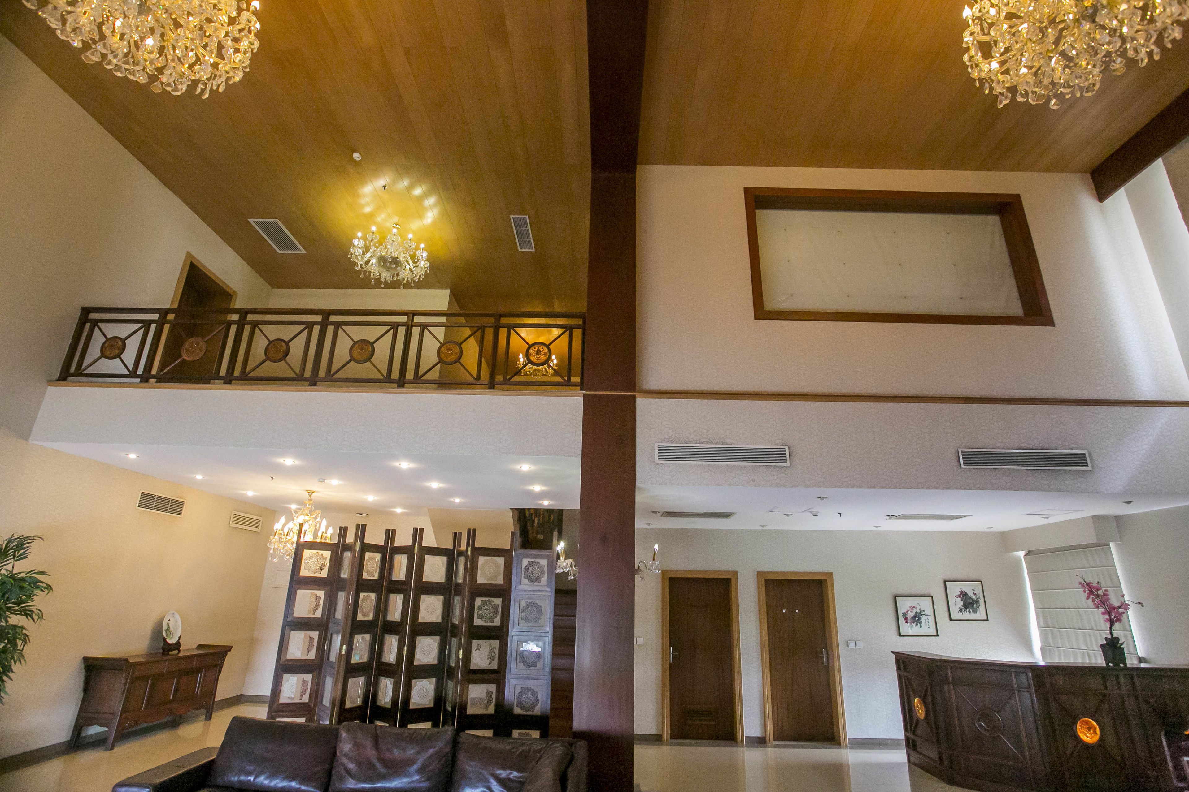 A spacious lobby with a wooden ceiling, a reception desk, a seating area, and a decorative wall with framed pictures.