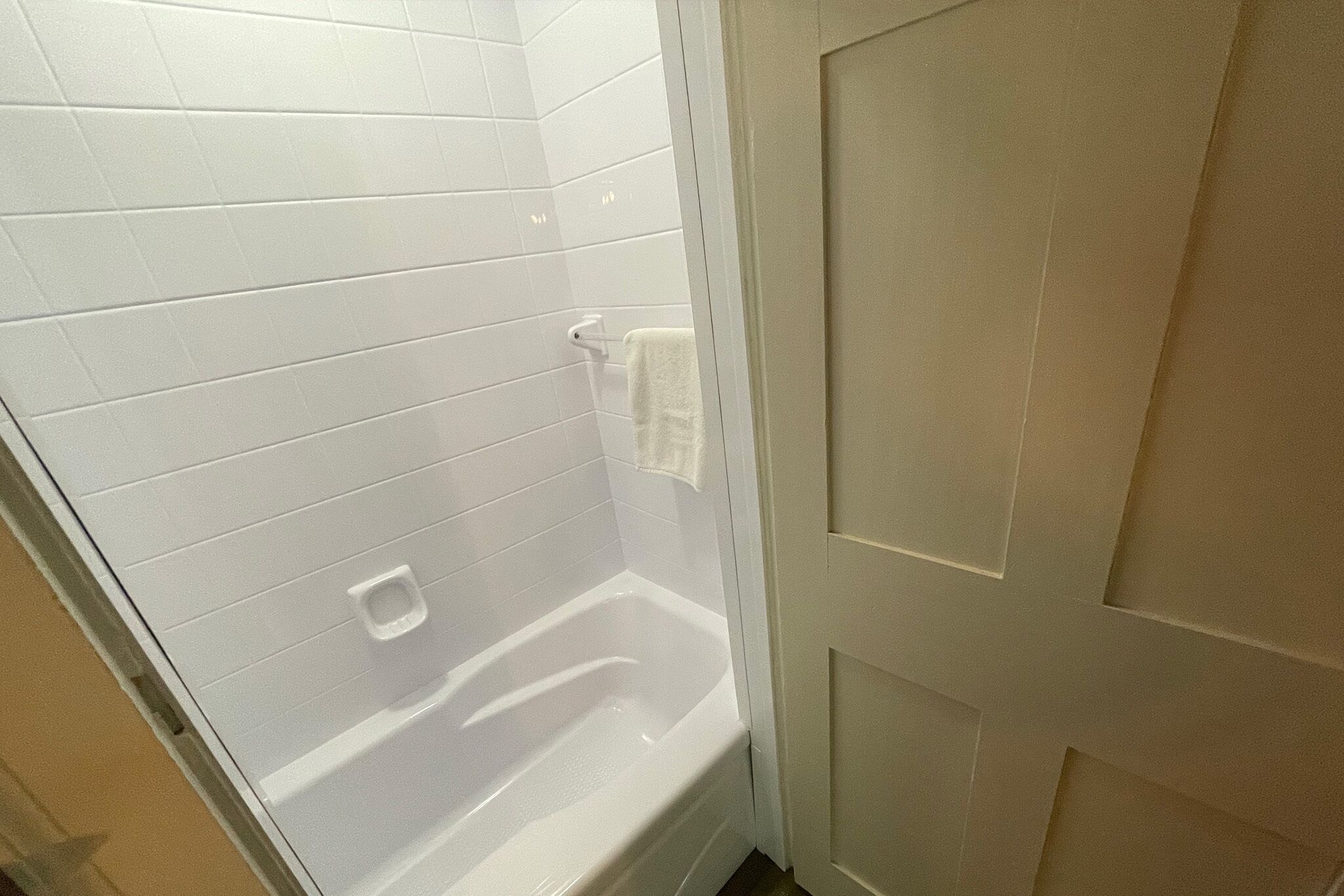Ein Badezimmer mit weiß gefliesten Wänden, einer weißen Badewanne und einer Tür.