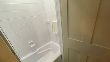 Ein Badezimmer mit weiß gefliesten Wänden, einer weißen Badewanne und einer Tür.