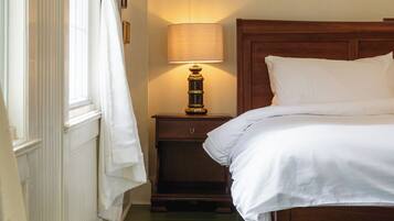 A bedroom with a wooden bed, a nightstand with a lamp, a window with curtains, and a green wooden floor.