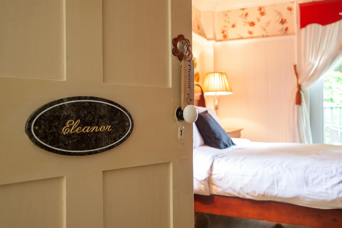 A hotel room with a bed, a lamp, and a door with a nameplate reading "Eleanor".
