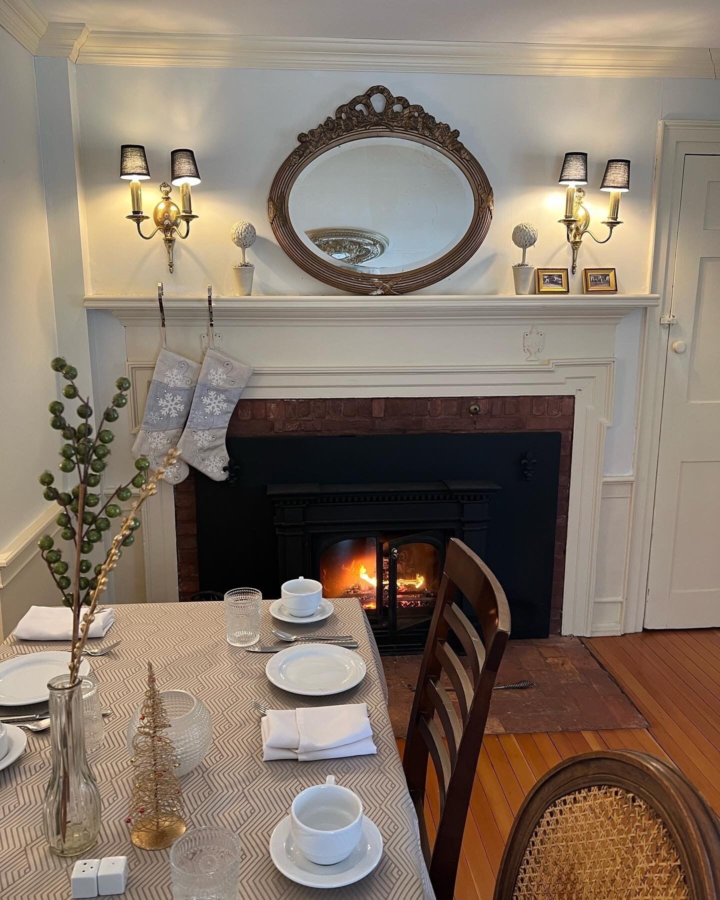 Une salle à manger avec une cheminée, une table dressée pour quatre personnes et un miroir au-dessus du manteau de cheminée.