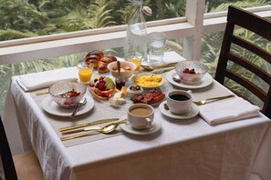 Une table de petit-déjeuner dressée avec des croissants, des fruits, des œufs brouillés et du café, offrant une vue sur la verdure environnante.