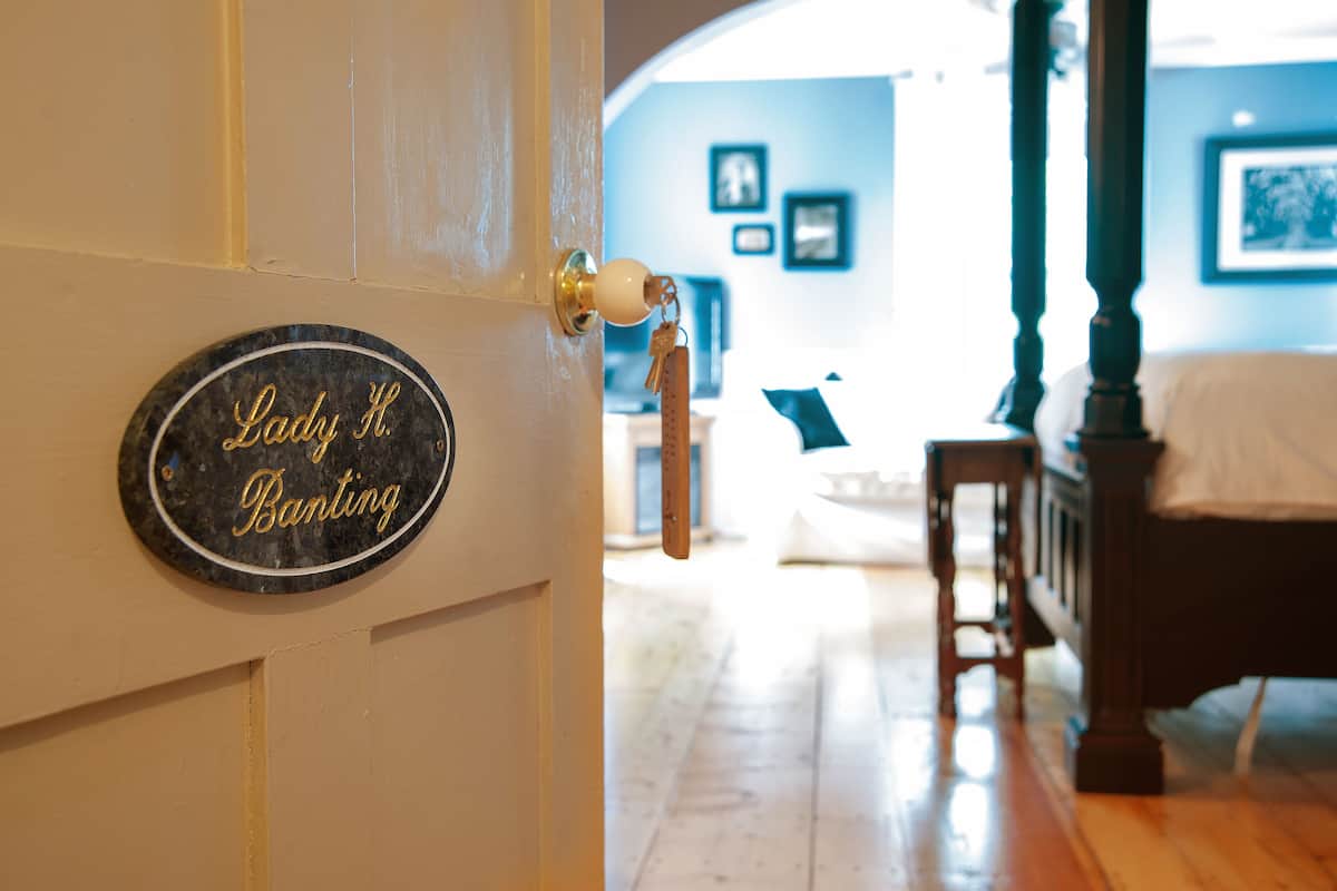 A room with a bed, a wooden chair, a wooden floor, a wall-mounted sign, and a door with a key in the lock.