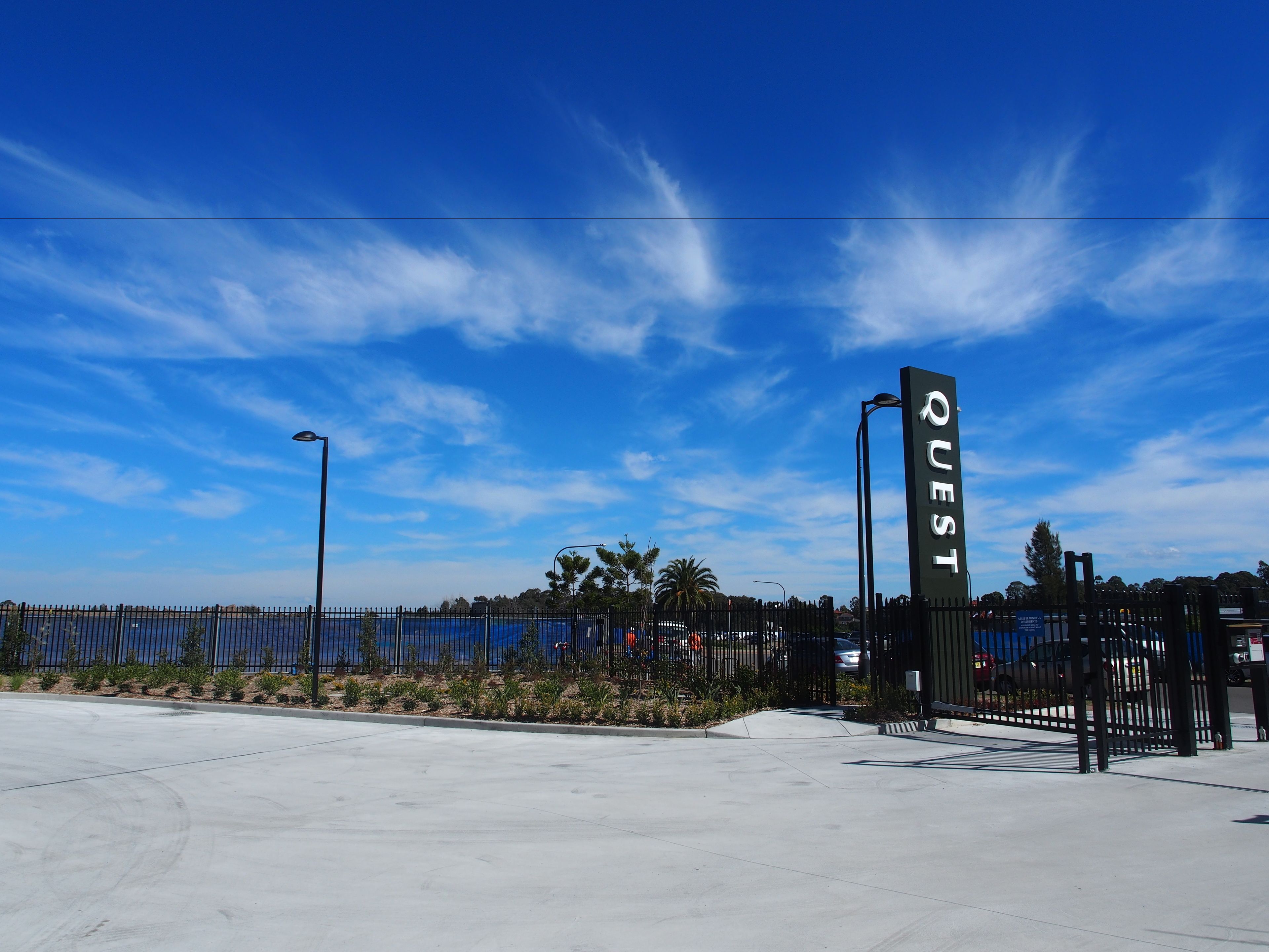 A parking lot with a fence and a sign that reads "QUEST".
