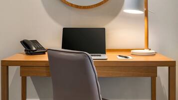 A wooden desk with a laptop, a phone, a lamp, and a chair.