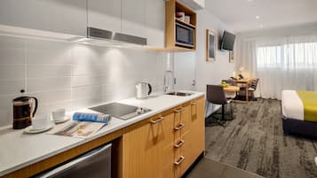 Quarto de hotel moderno com cozinha compacta, área de refeições e uma cama.