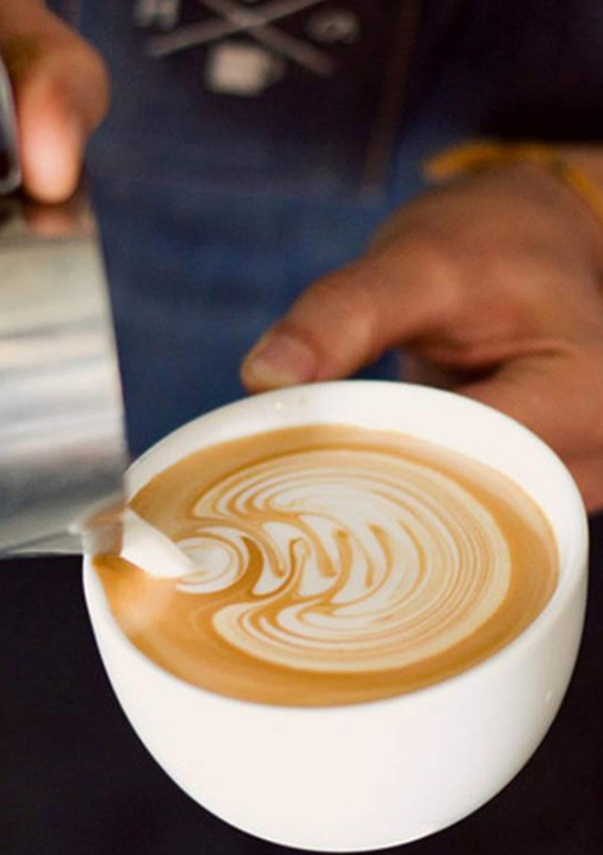 A person pouring steamed milk into a cup of coffee, creating a latte art pattern.