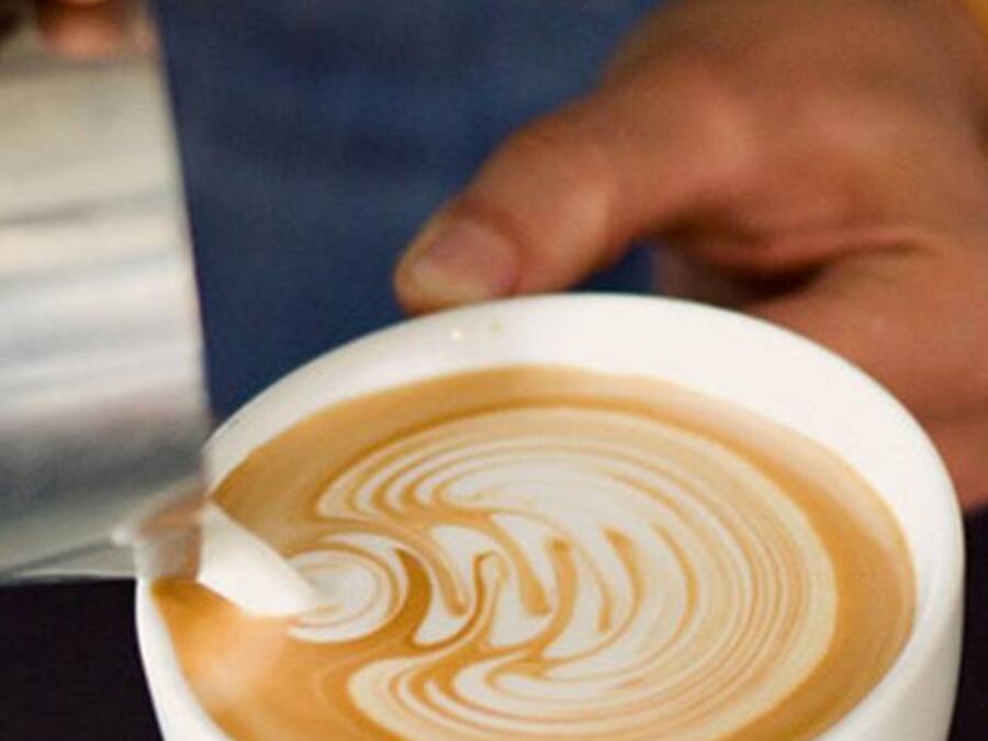 A person pouring steamed milk into a cup of coffee, creating a latte art pattern.