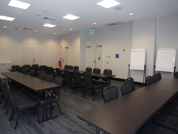 Un salón de conferencias con largas mesas y sillas, una pizarra y un extintor.