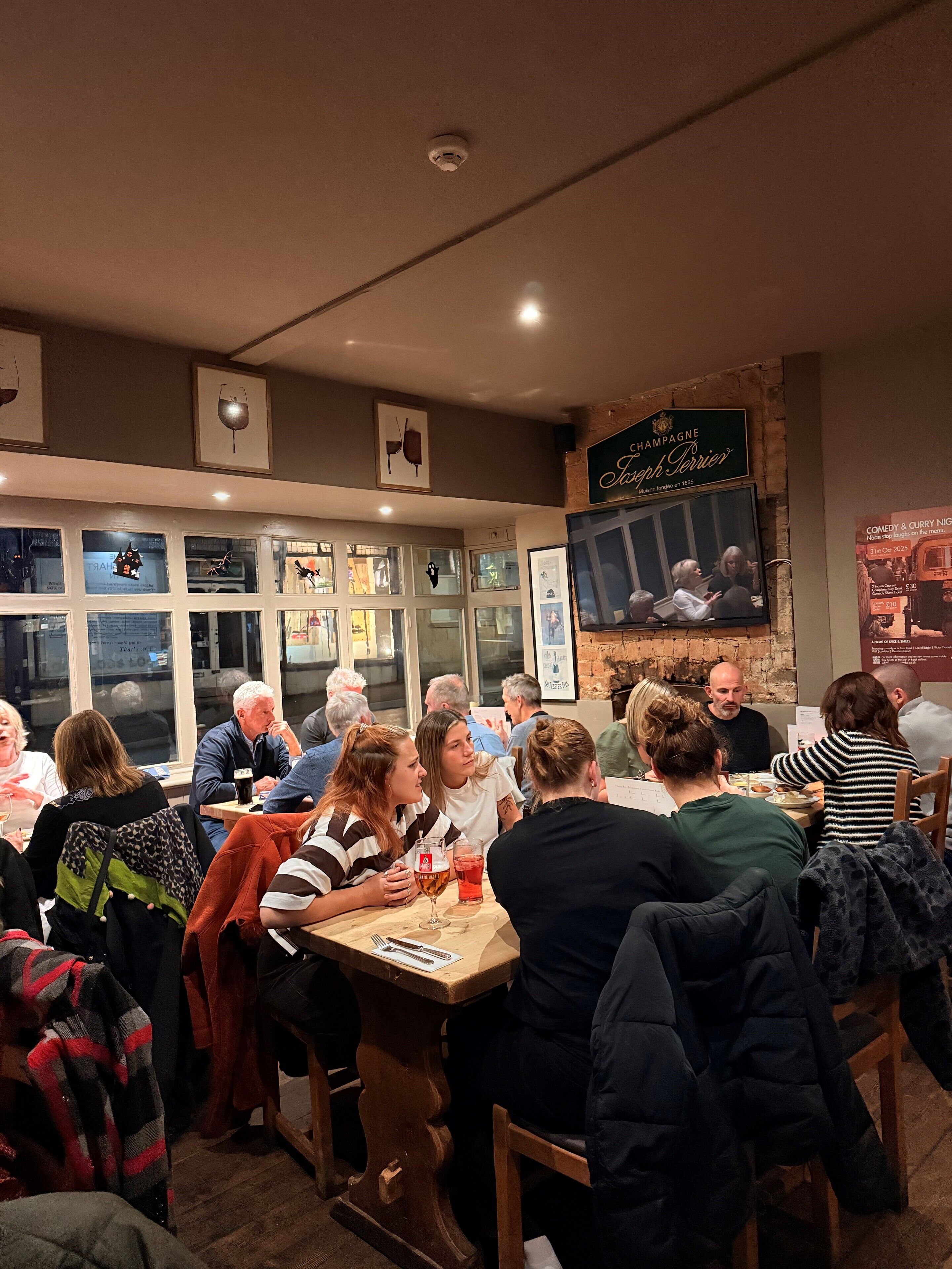 A restaurant interior with patrons seated at tables, a television mounted on the wall, and framed artwork on the walls.