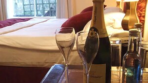 A bed with white linens, a red pillow, and a bottle of champagne on a bedside table. - The White Hart Inn (Cheltenham)