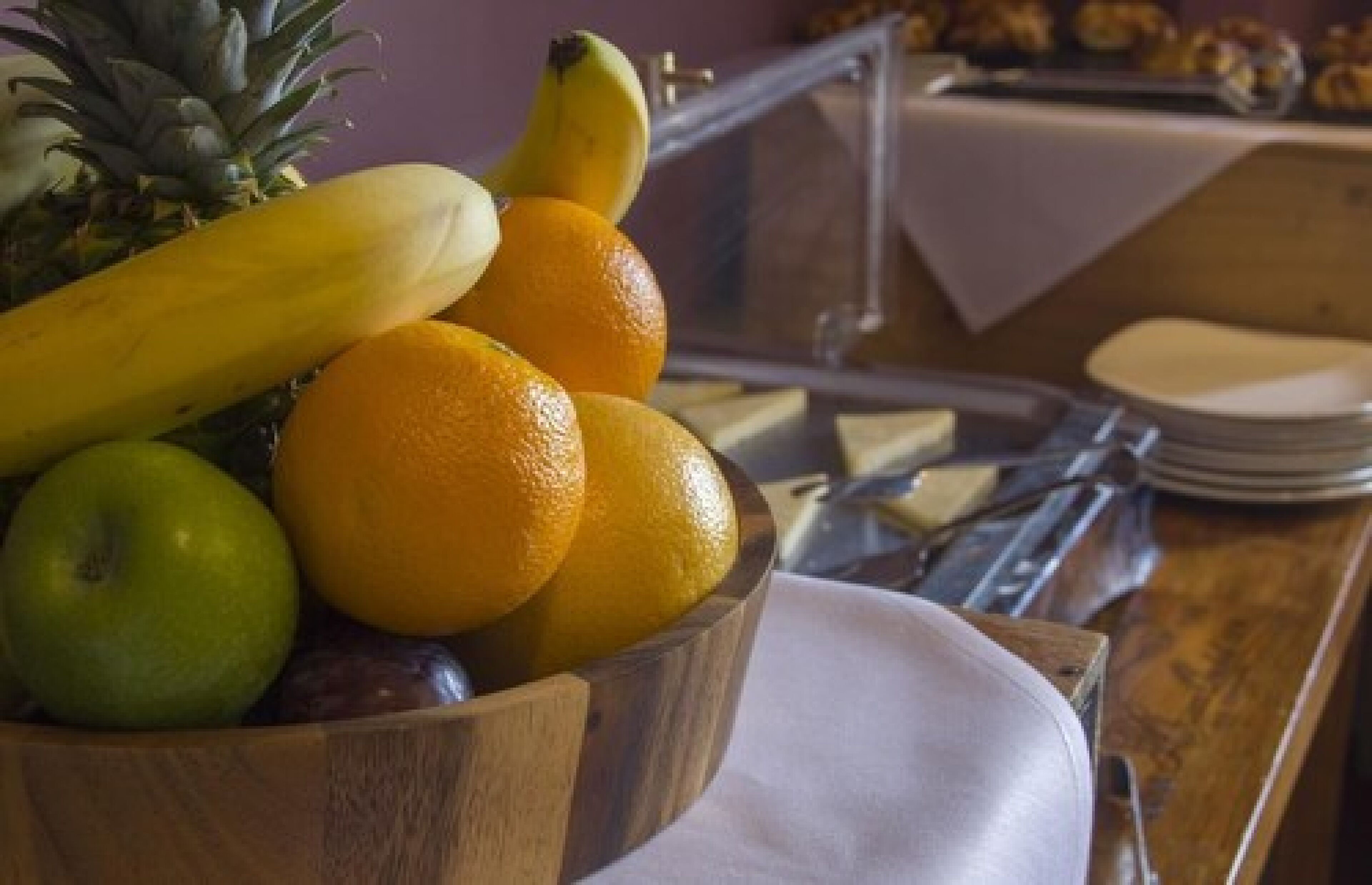 A wooden bowl filled with fruits including bananas, oranges, and a pineapple.
