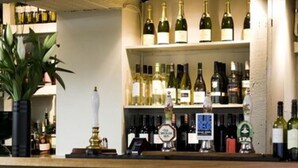 A bar area with shelves of wine bottles, a clock, and a potted plant. - The White Hart Inn (Cheltenham)