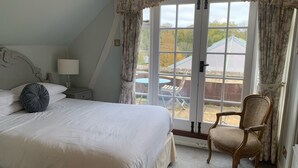 A bedroom with a large bed, a chair, a nightstand, and a window with curtains. - The White Hart Inn (Cheltenham)
