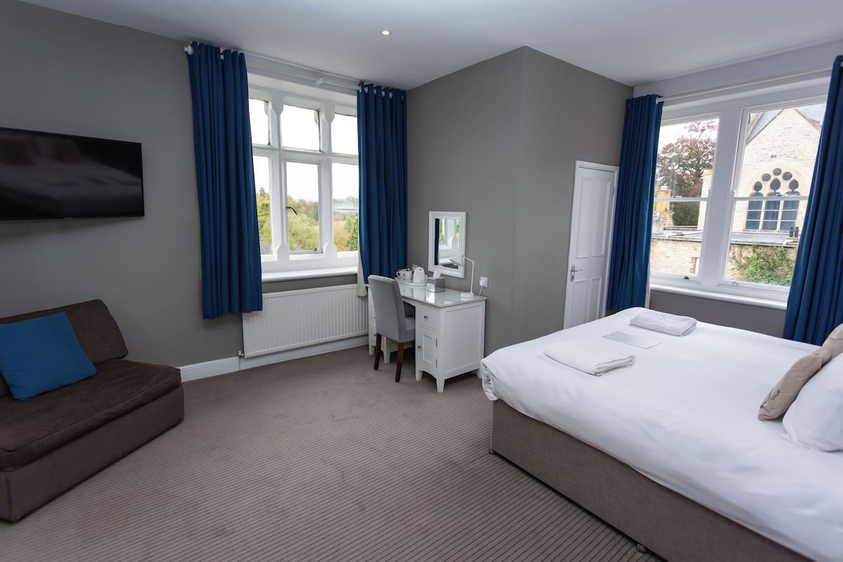 A hotel room with a bed, a desk, a TV, and a window with curtains.
