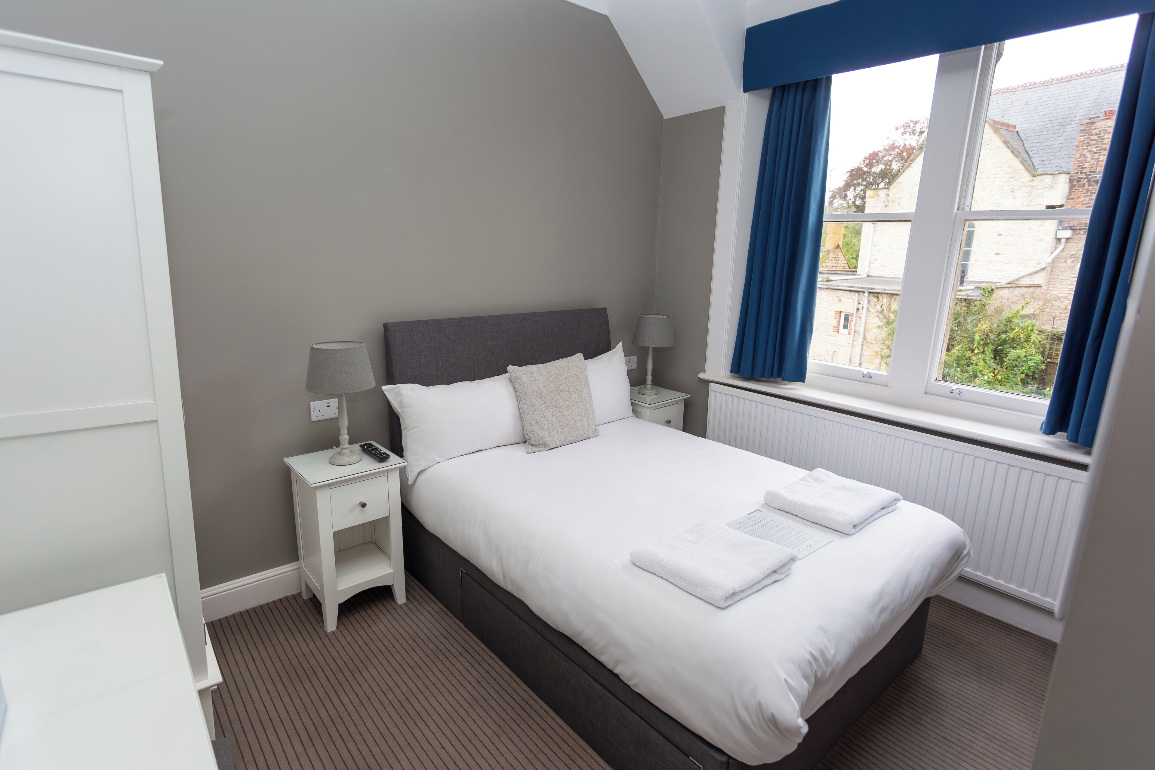 A neatly arranged bedroom with a large bed, bedside tables, and a window with curtains.