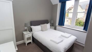 A neatly arranged bedroom with a large bed, bedside tables, and a window with curtains.