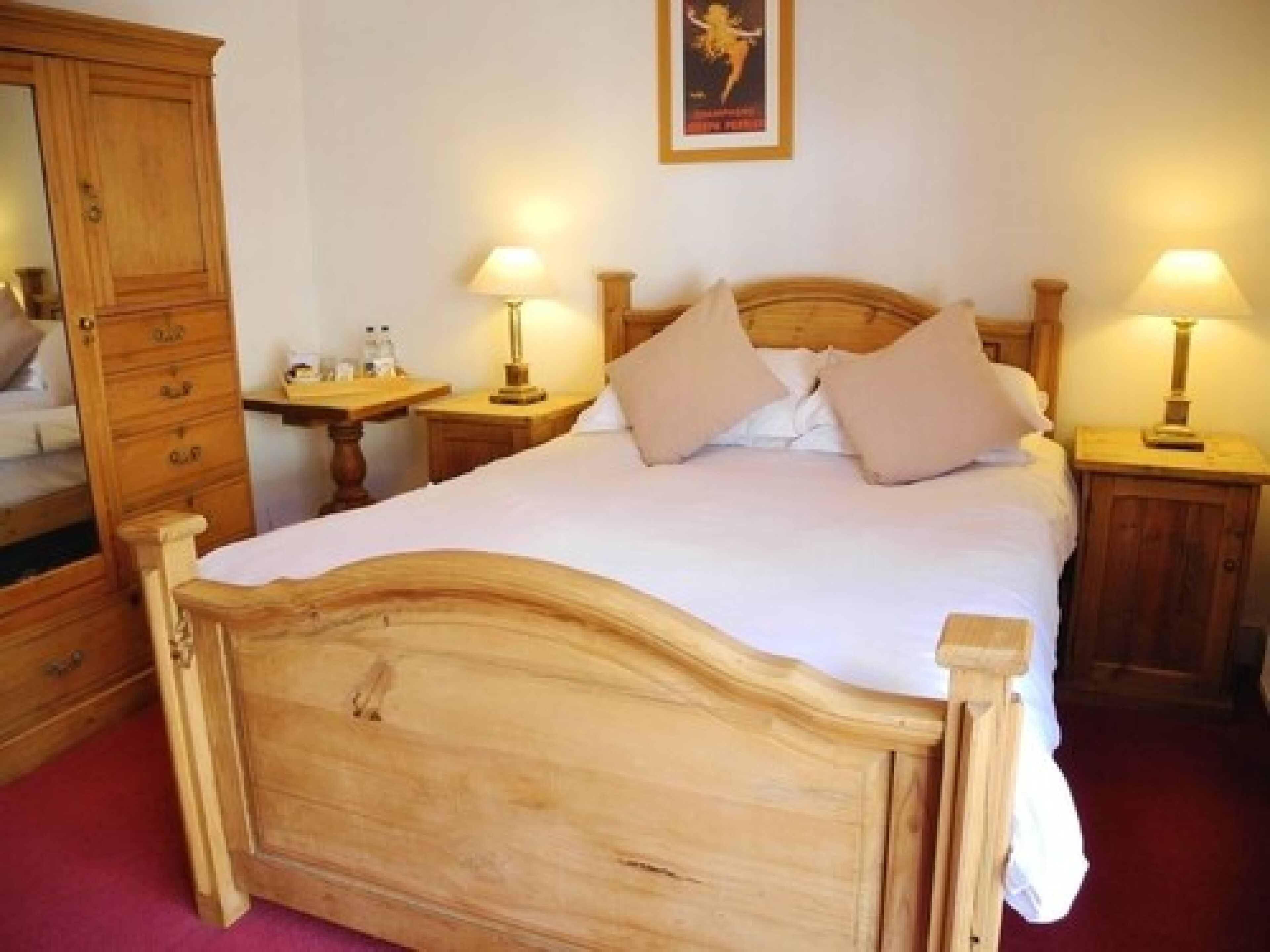 Una cama con dosel de madera, con sábanas blancas, dos mesitas de noche con lámparas y un armario de madera.