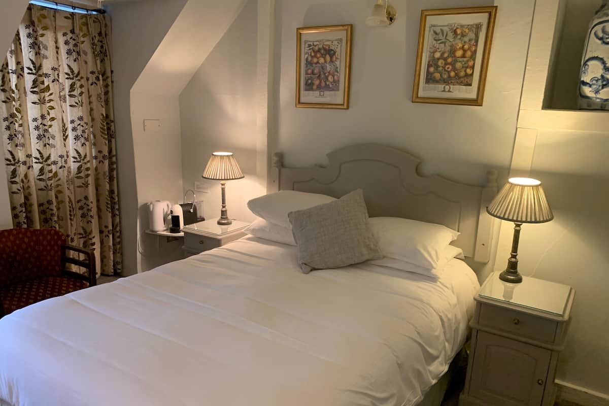 A neatly made bed with white linens, two bedside lamps, a chair, and two framed fruit paintings on the wall.