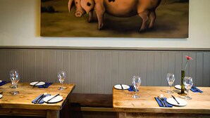 A restaurant with tables set for dining, a painting of a pig on the wall, and a flower on one table. - The White Hart Inn (Cheltenham)