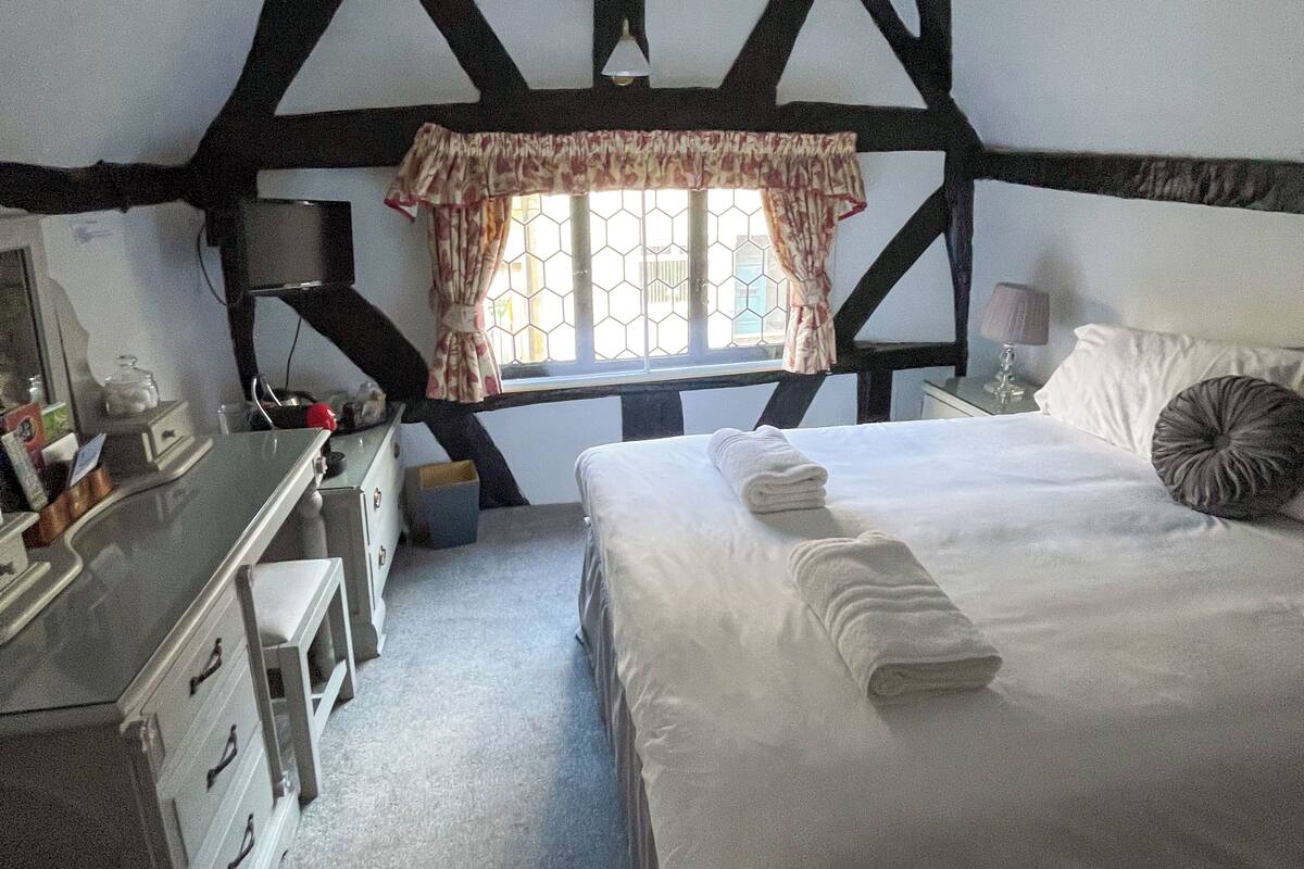 A bedroom with a bed, a desk, a chair, a window with curtains, and a lamp.
