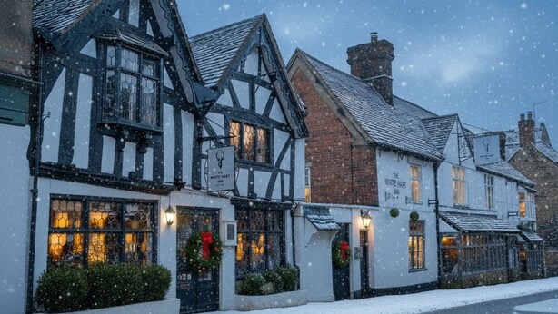 A traditional Tudor-style inn with a signboard, a well-lit entrance, and snow on the ground. - The White Hart Inn (Cheltenham)
