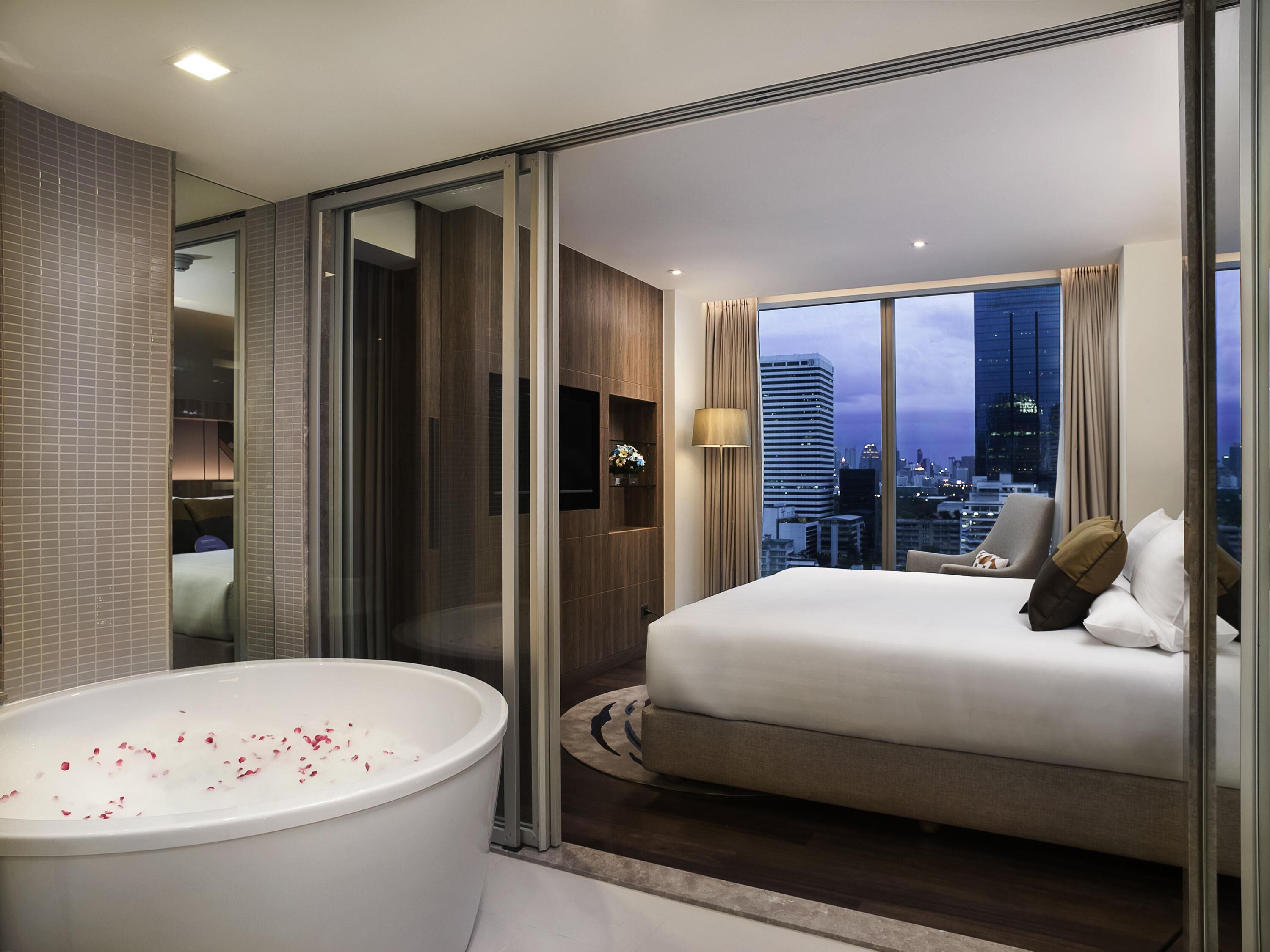 Una habitación de hotel moderna con una cama grande, una bañera y vistas a la ciudad.
