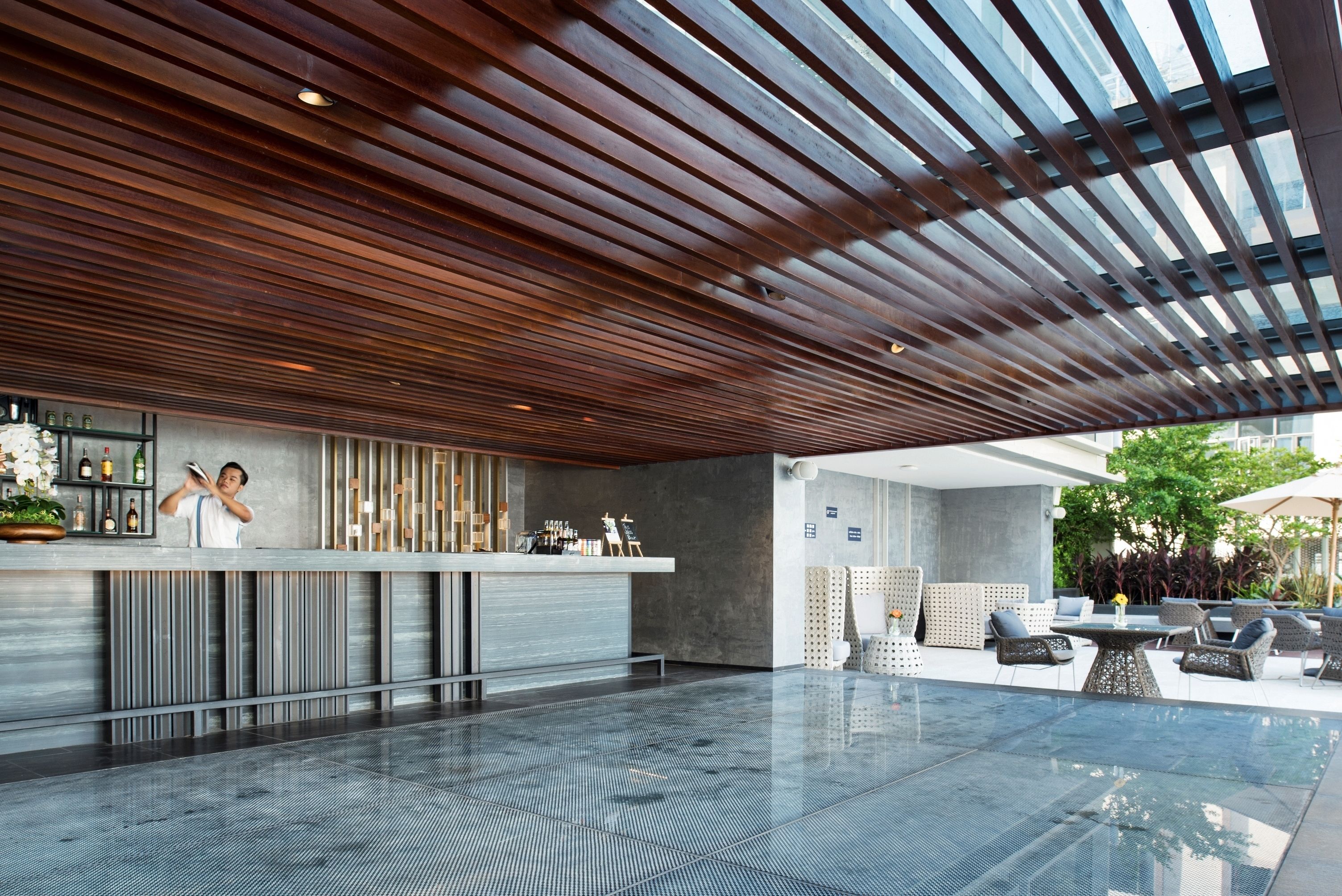 A modern bar area with a long counter, seating area with tables and chairs, and a glass-enclosed outdoor space.