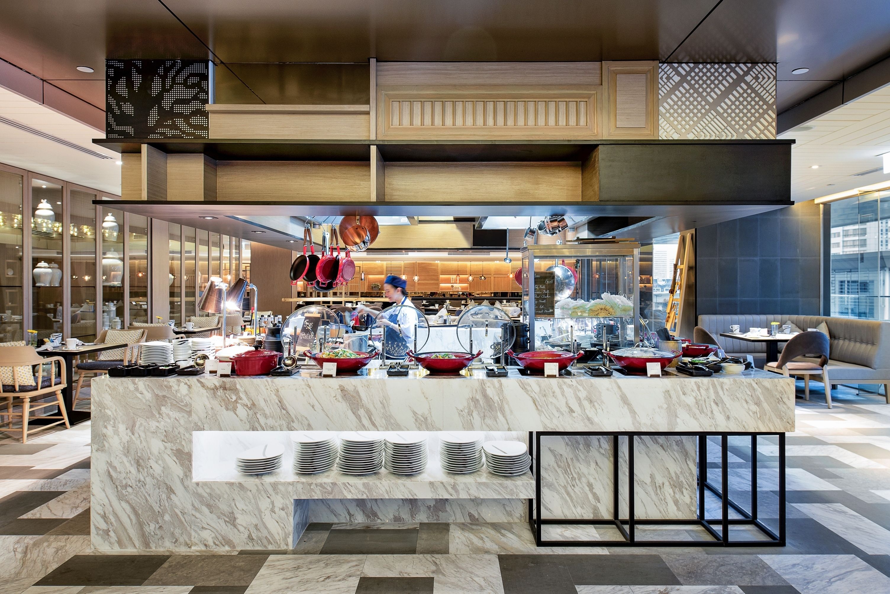 A modern kitchen area with marble countertops, a buffet setup with various dishes, and a seating area with tables and chairs.