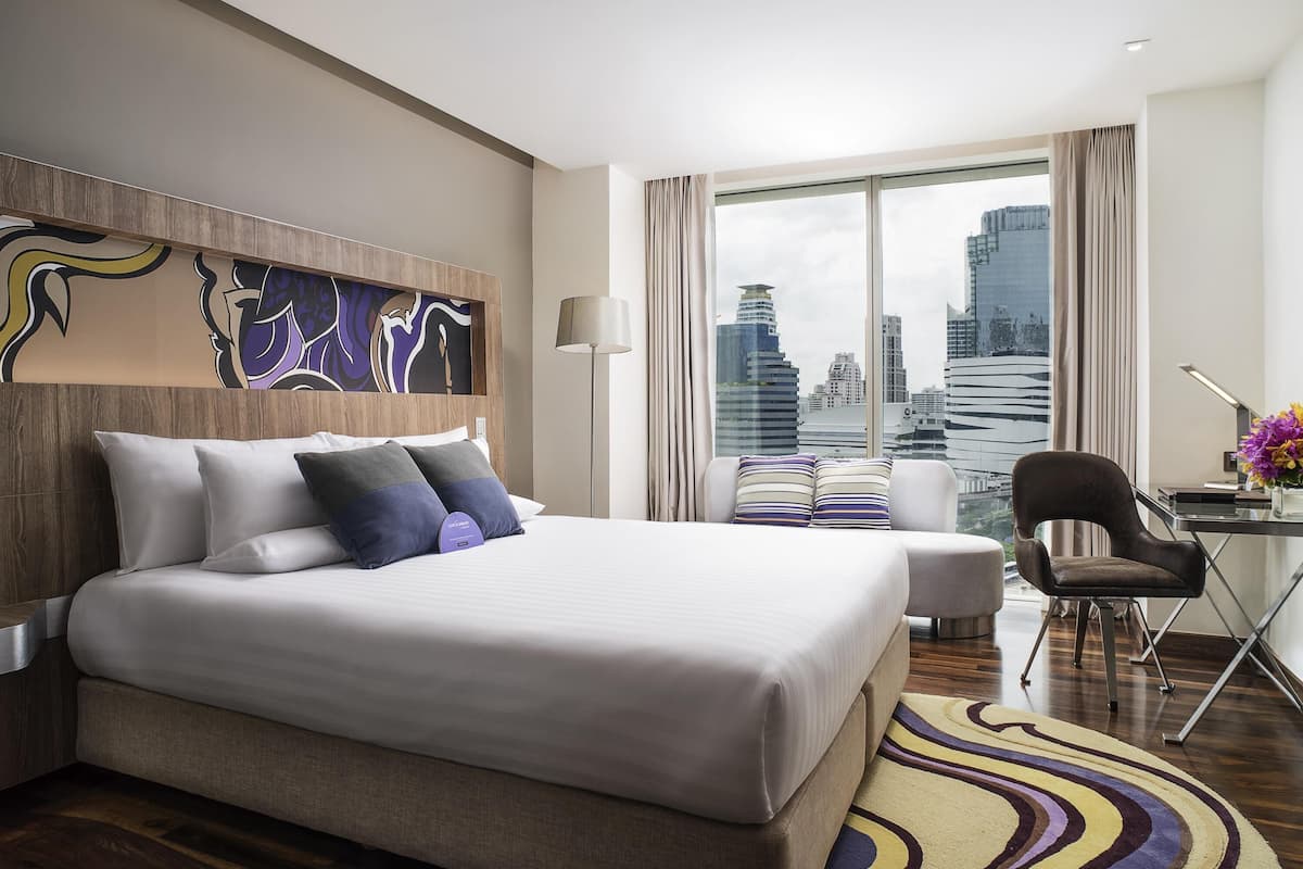 Habitació d'hotel moderna amb un llit gran, un escriptori i vista a l'horitzó de la ciutat.
