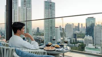 A man dining at a table with a city view, including tall buildings and a sunset.