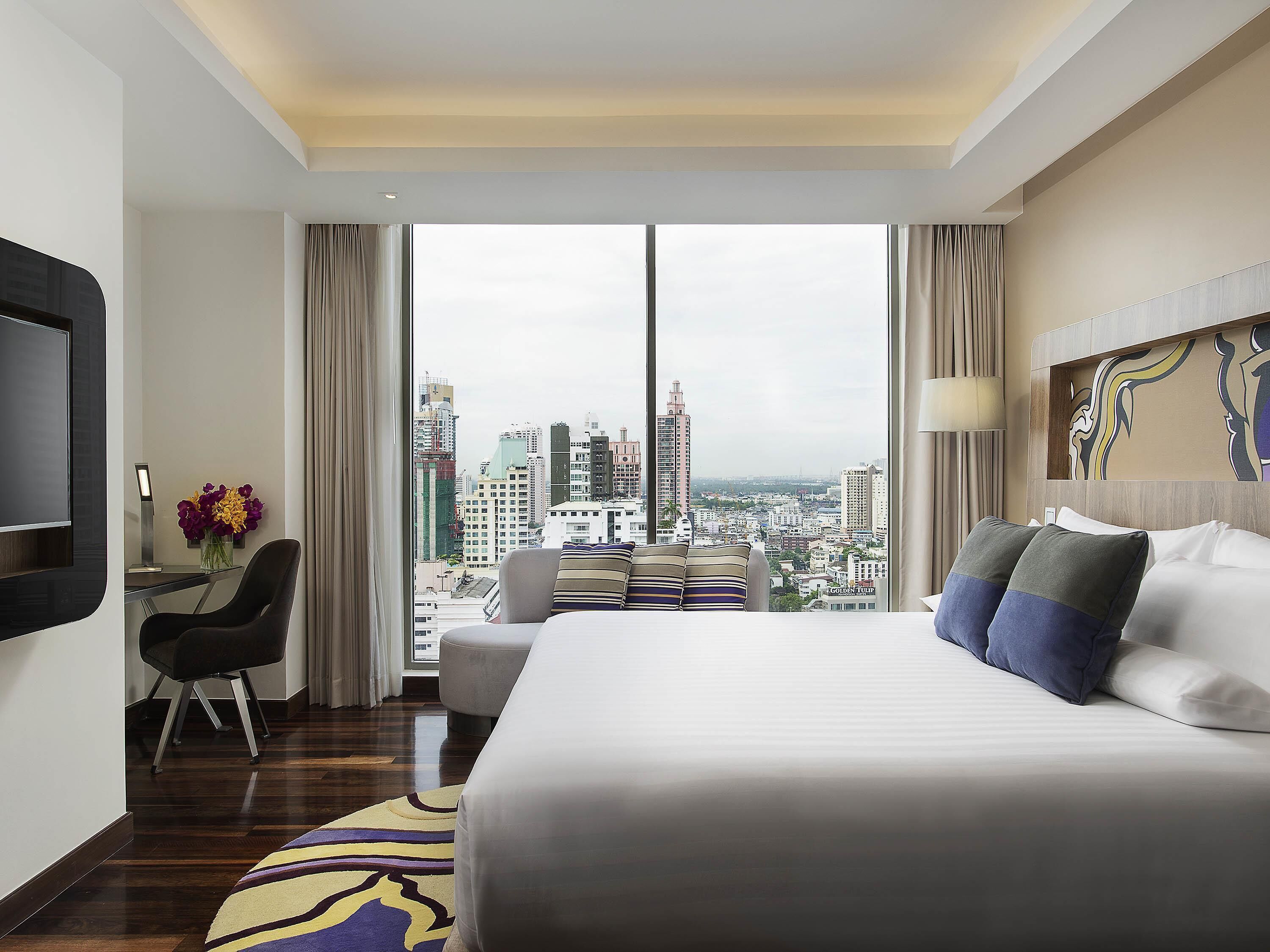 Habitación de hotel con una cama grande, un escritorio con silla, televisión y vista a la ciudad.