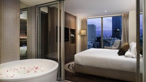 Een moderne hotelkamer met een groot bed, een badkuip en uitzicht over de stad.