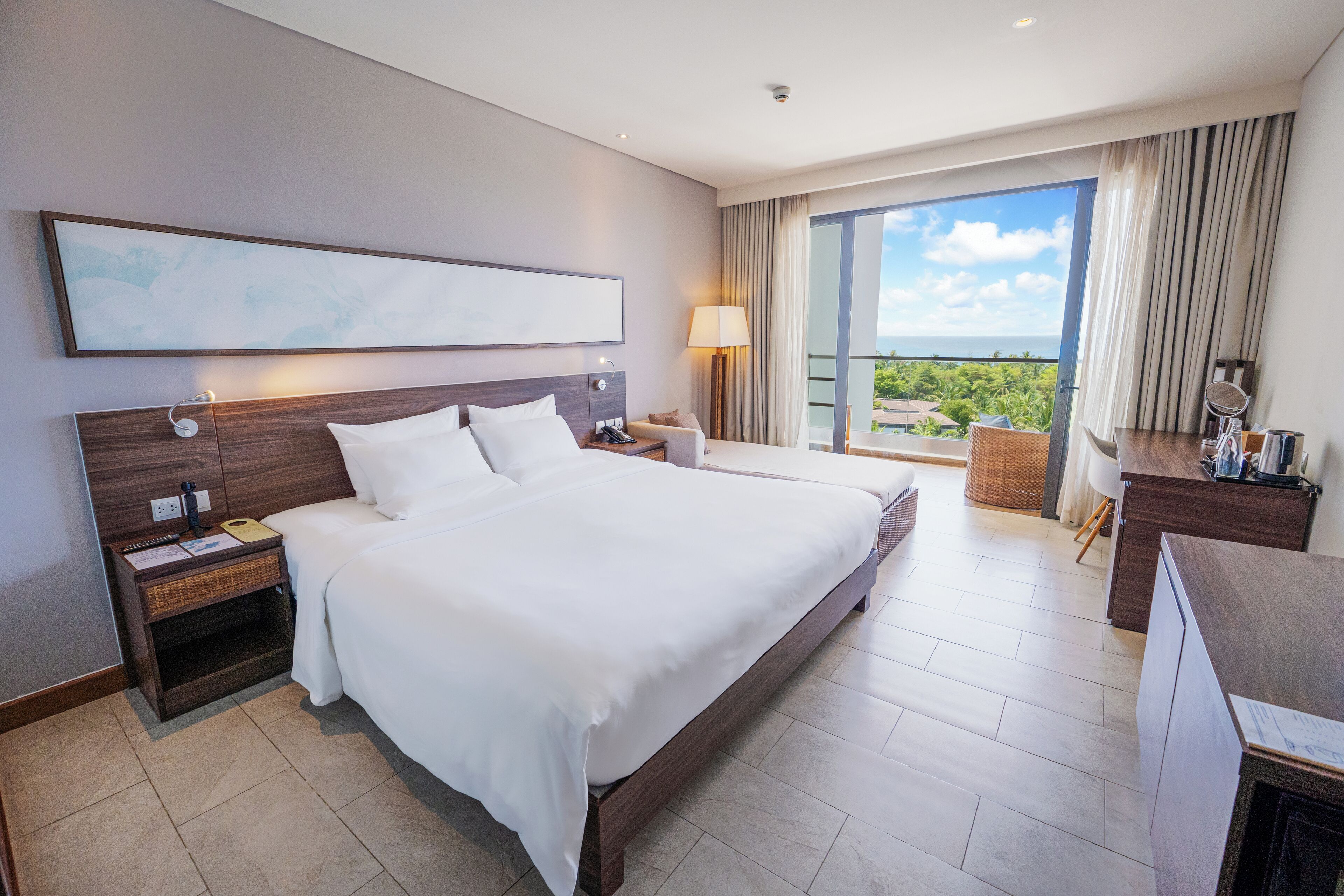 Una habitación de hotel moderna con una cama grande, una mesita de noche, un escritorio y un balcón con vistas.
