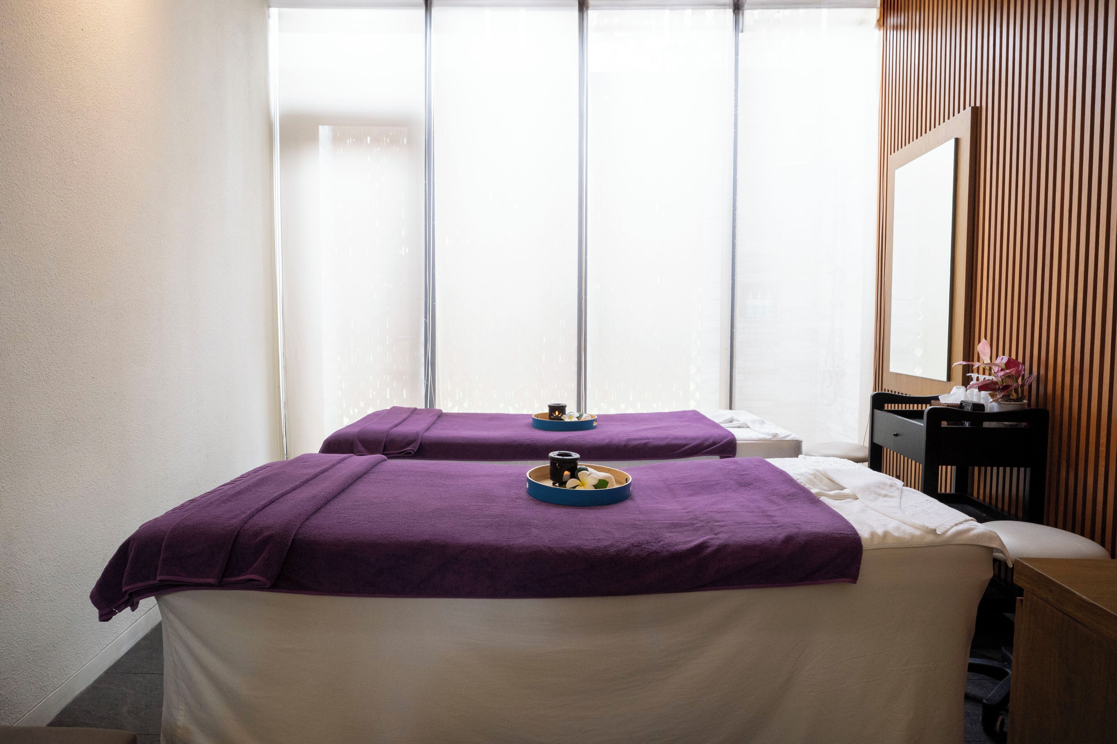 A room with two beds covered in purple towels, a wooden headboard, and a mirror on the wall.