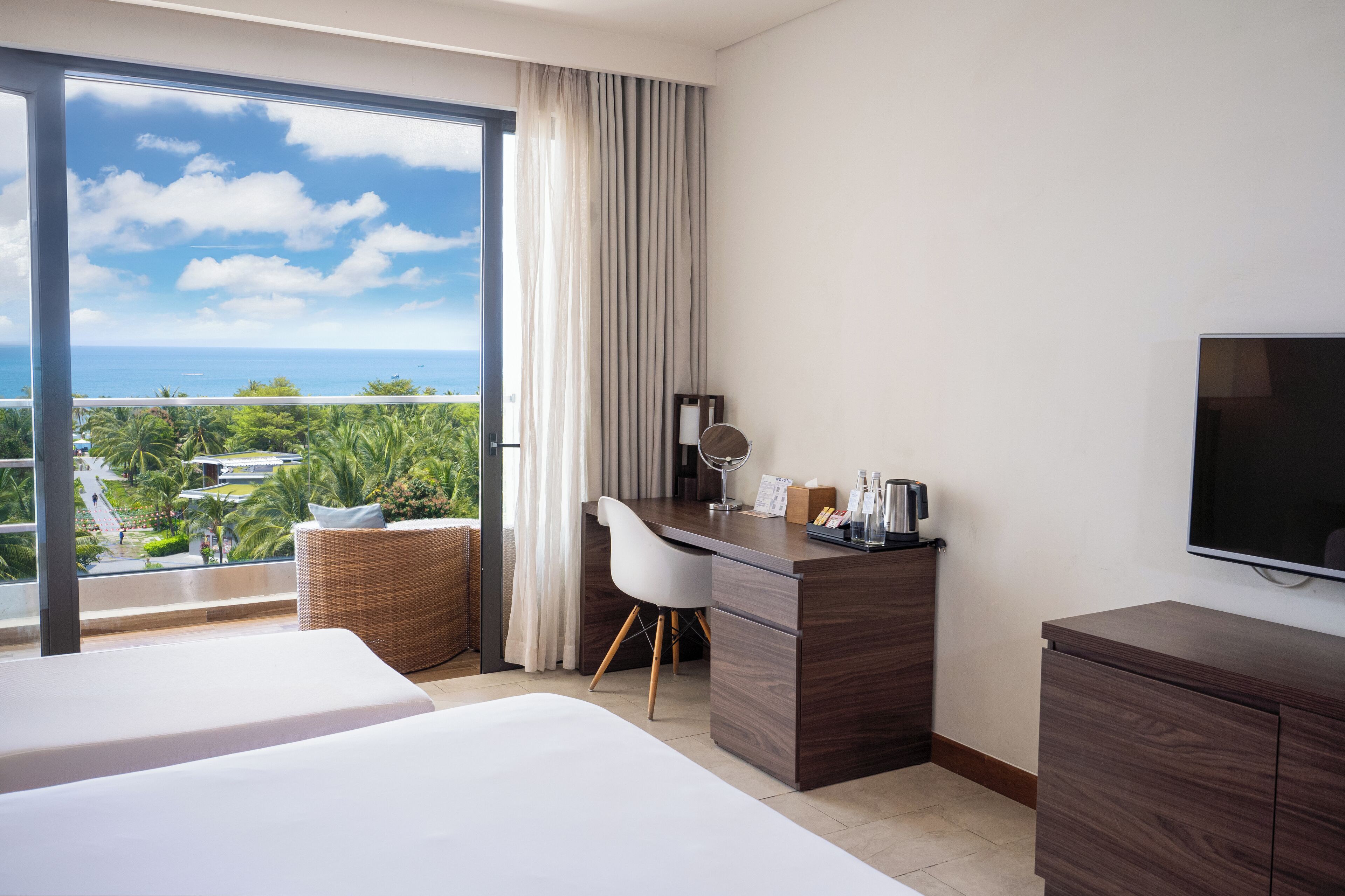 A hotel room with a balcony, a desk, a TV, and a bed.
