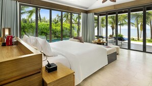 A hotel room with a large bed, a bedside table with a phone, a view of the beach and palm trees through large windows.
