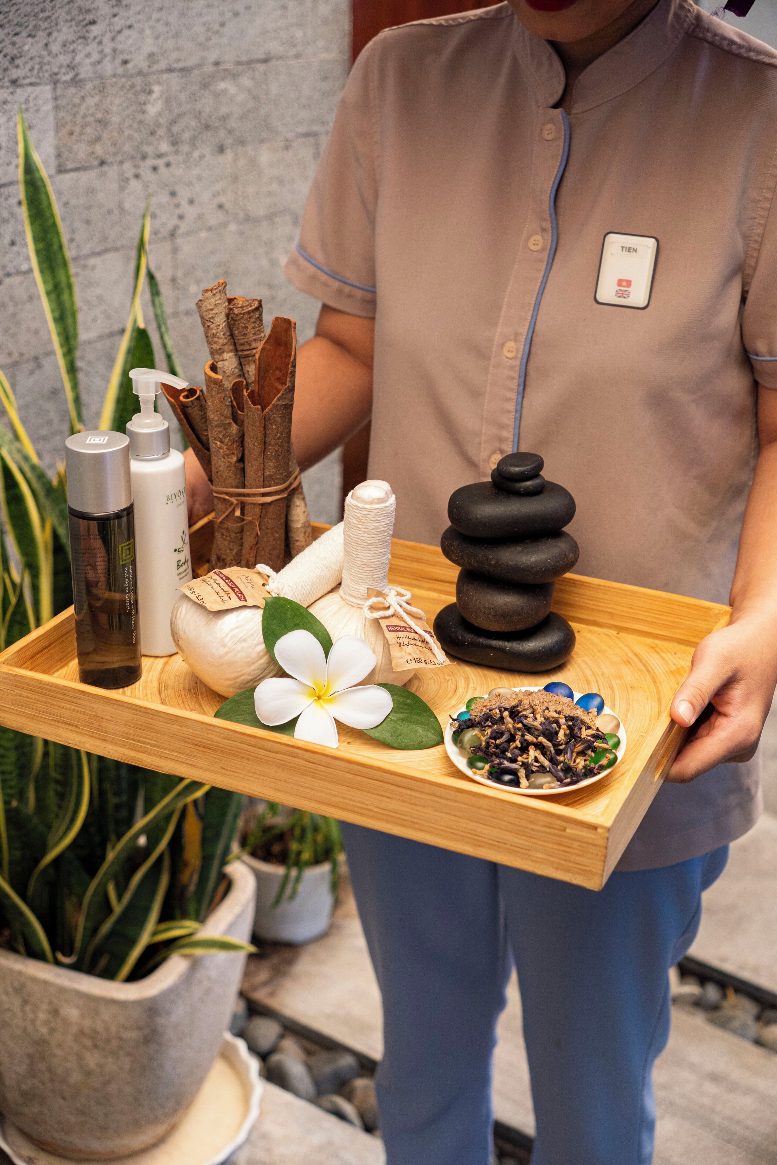 Ein Tablett mit verschiedenen Wellnessprodukten, darunter Flaschen, eine Steinsammlung und eine Blume.