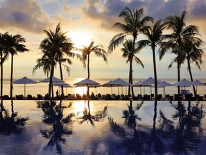 A poolside area with lounge chairs and umbrellas, palm trees, and a sunset view. - Novotel Phu Quoc Resort (Phu Quoc)