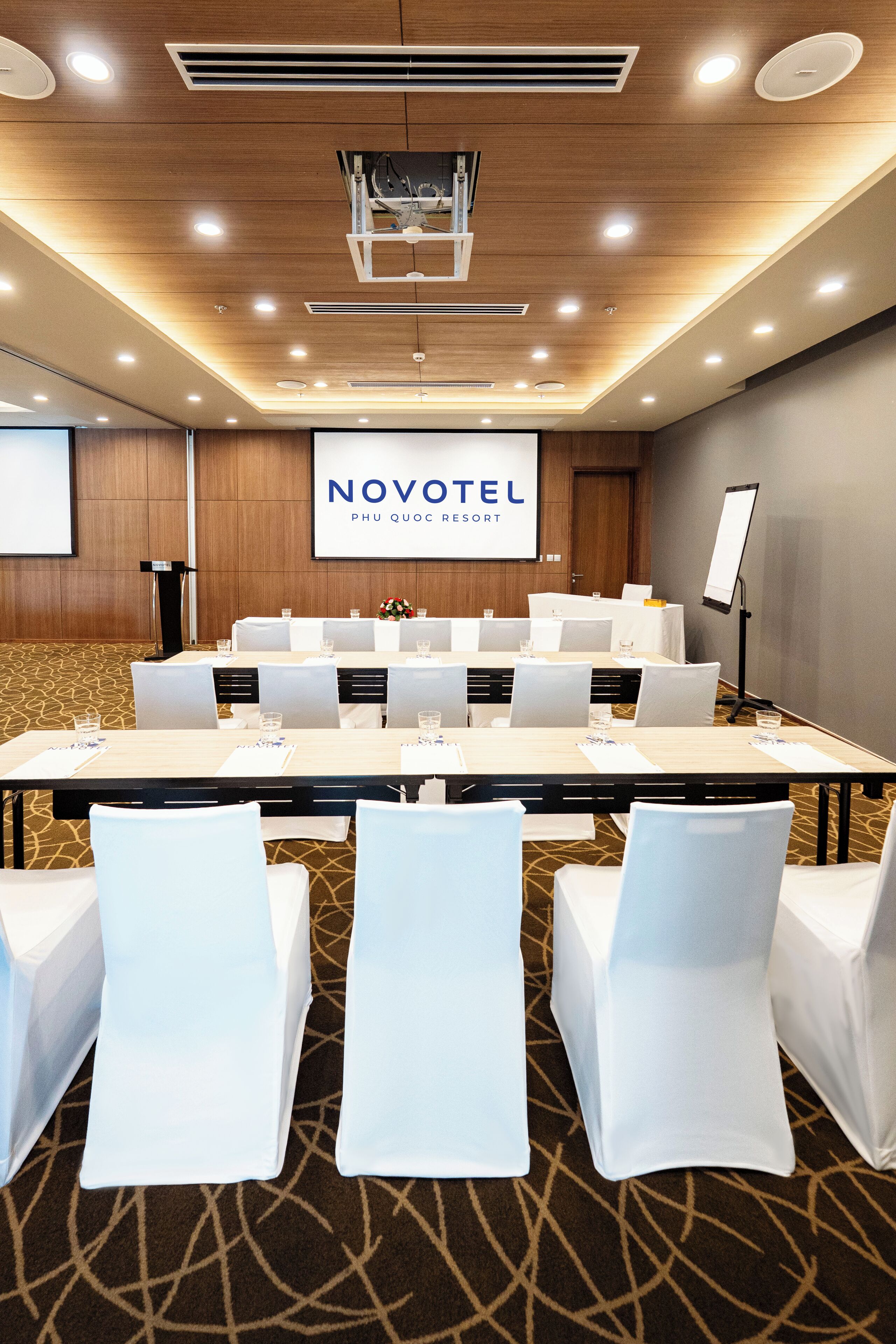 A conference room with a long table, white chairs, and a projector screen displaying 'NOVOTEL PHU QUOC RESORT'.