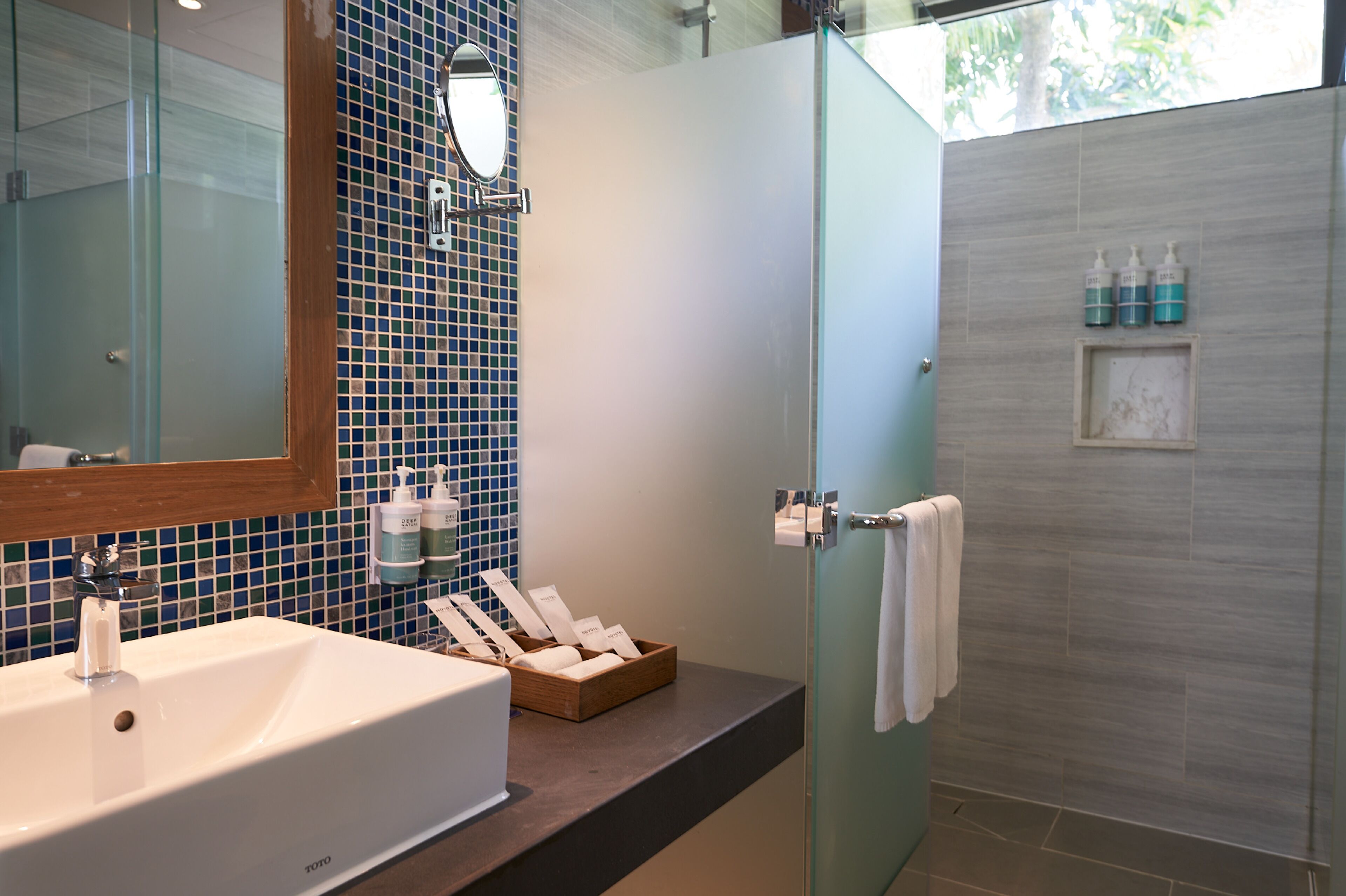 A bathroom with a white sink, a glass shower enclosure, and toiletries on the counter.