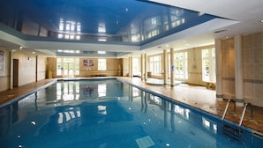 A large indoor swimming pool with clear water, surrounded by tiled walls and columns, and large windows allowing natural light. - Shaw Hill Golf Resort & Spa Hotel (Chorley)
