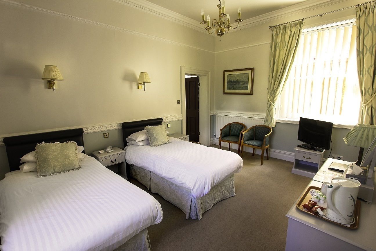A hotel room with two single beds, a desk with a coffee maker, a chair, a television, and a painting on the wall.