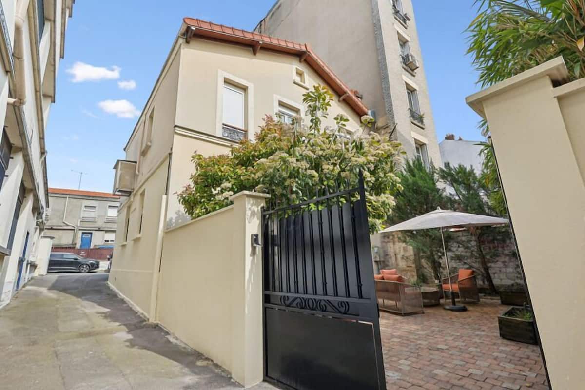 A narrow alleyway with a gated entrance, a paved pathway, and a patio area with outdoor furniture.